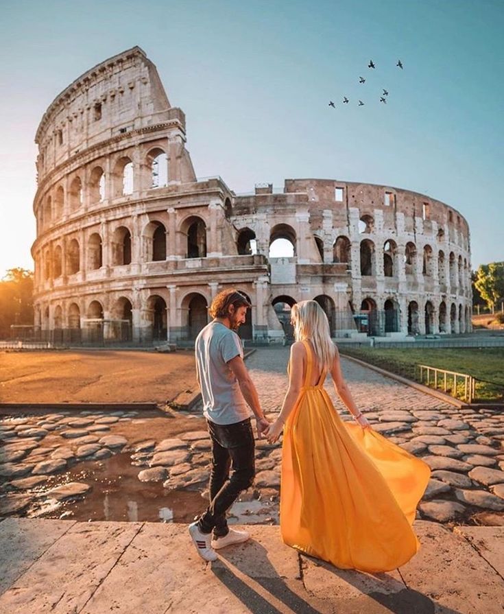 a man and woman walking in front of the colossion with their arms around each other