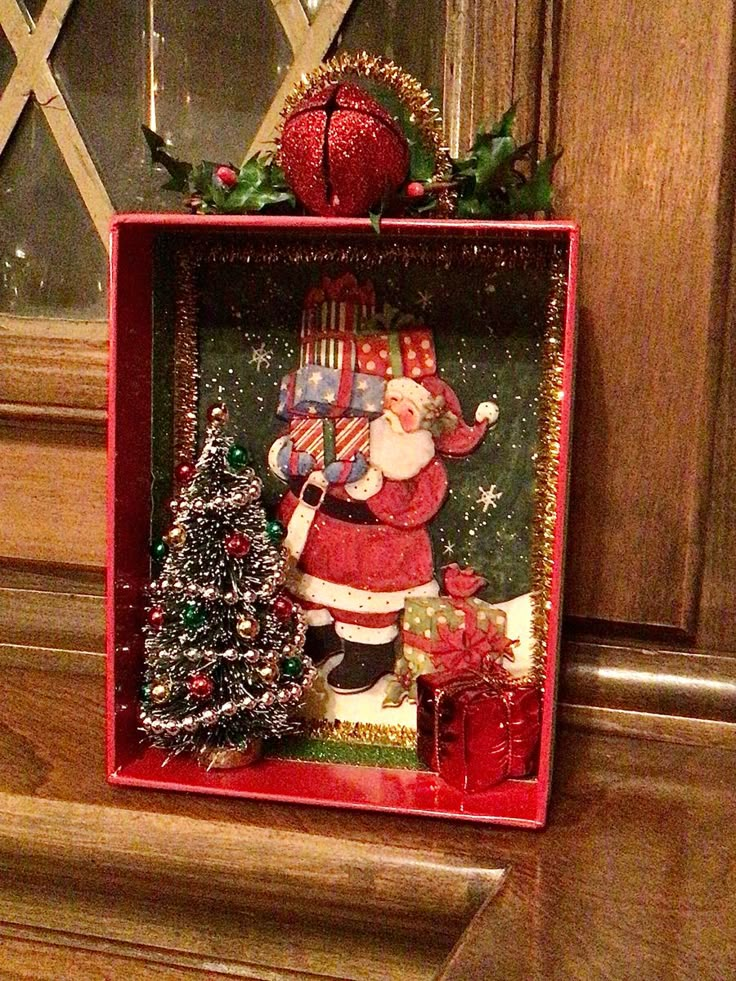 a christmas decoration in a red box with santa clause holding a bag and presents on it