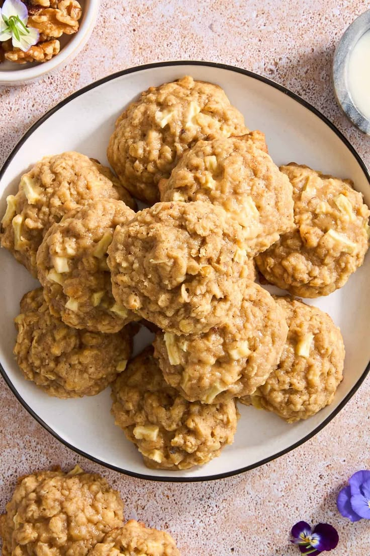 a white plate topped with oatmeal cookies next to a bowl of nuts