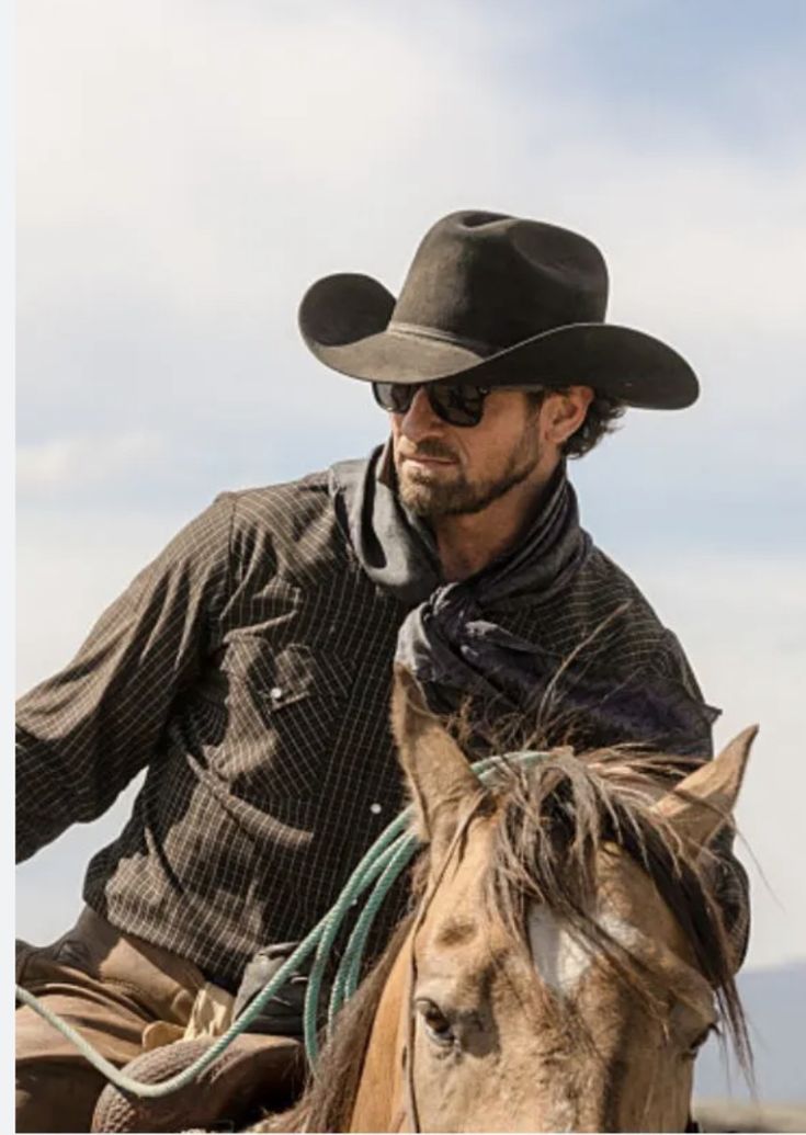 a man riding on the back of a brown horse wearing a cowboy hat and sunglasses