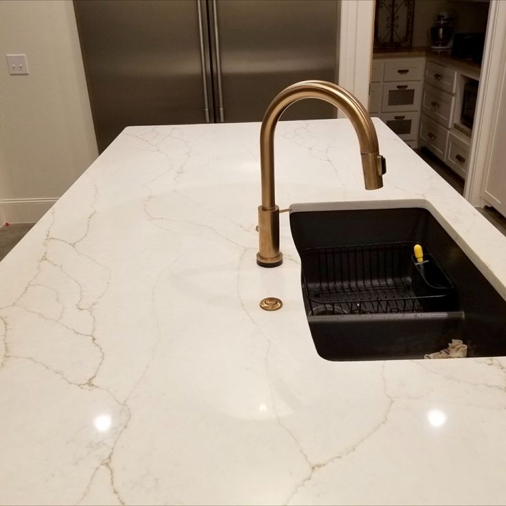 a kitchen sink with a faucet in the middle and marble counter top next to it