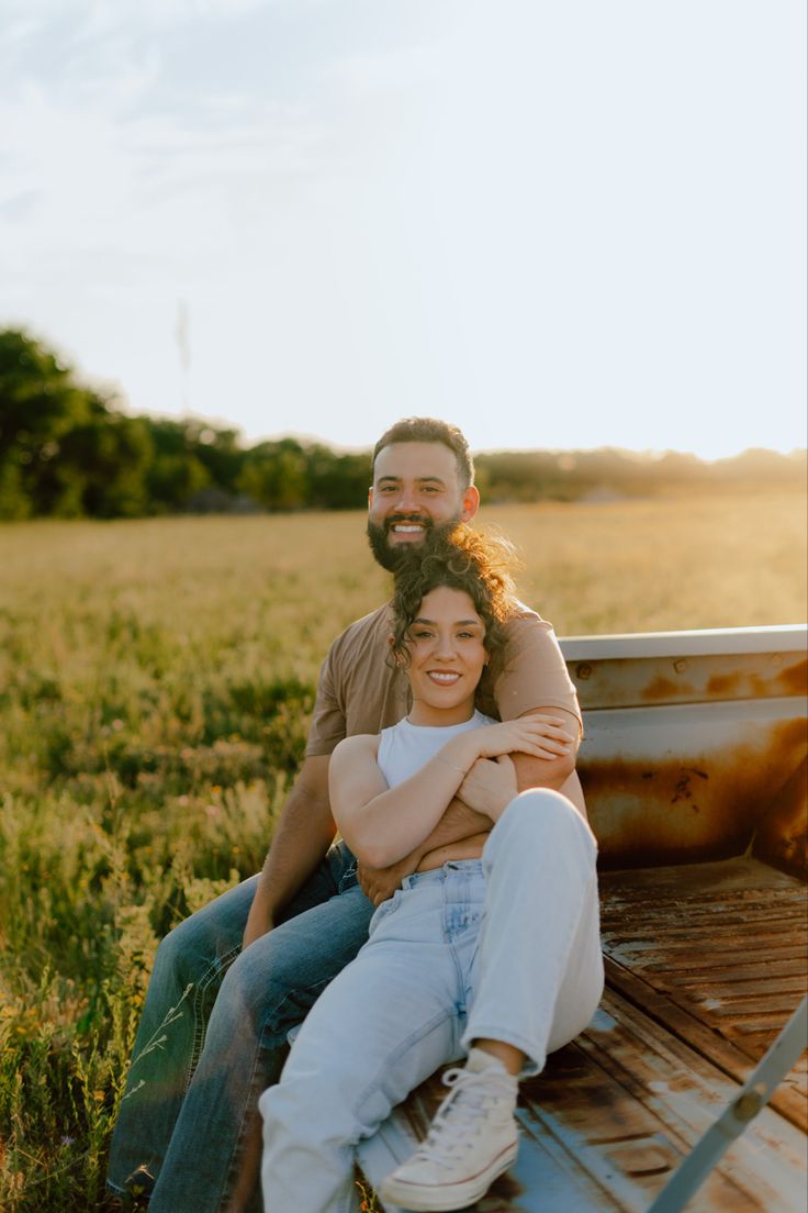 a man and woman sitting on the back of a truck in an open grassy field