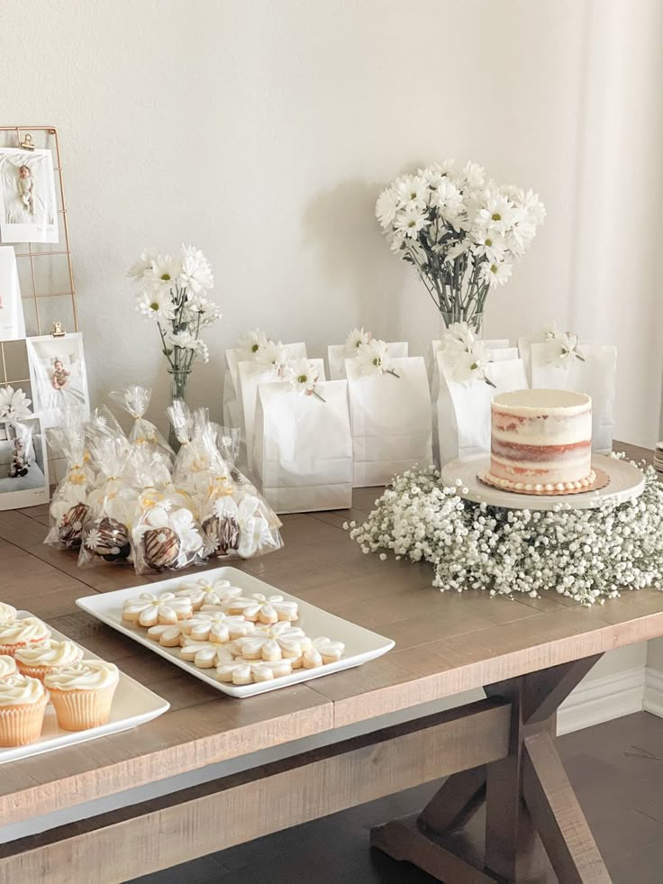 a table topped with cakes and cupcakes on top of a wooden table covered in white flowers