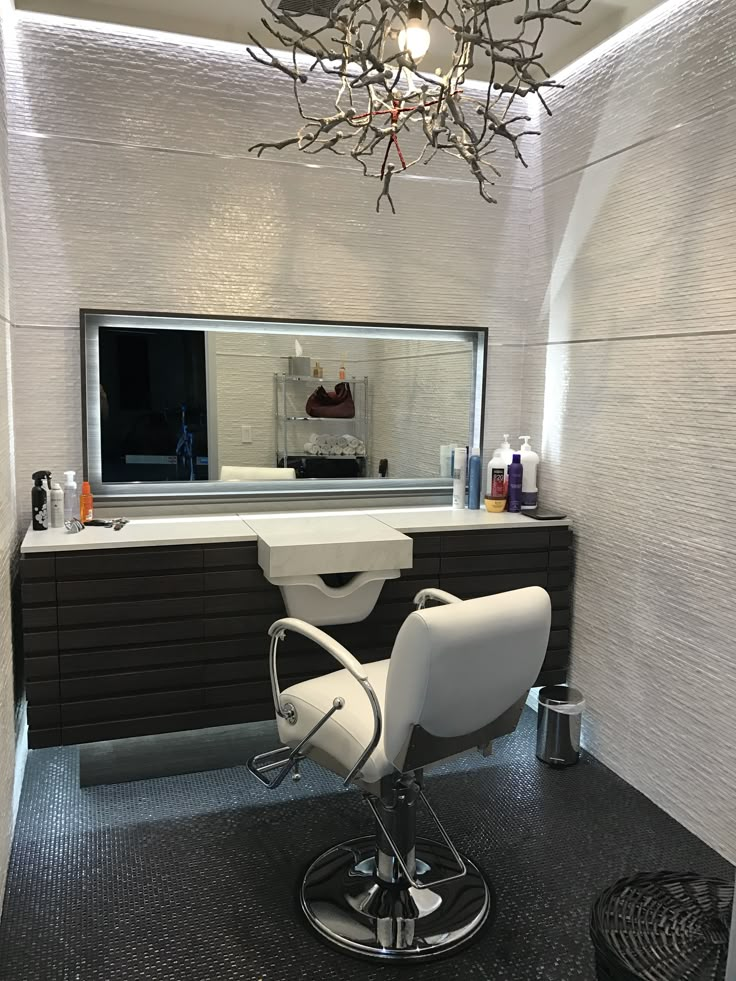 a white chair sitting in front of a mirror on top of a black counter next to a hair dryer