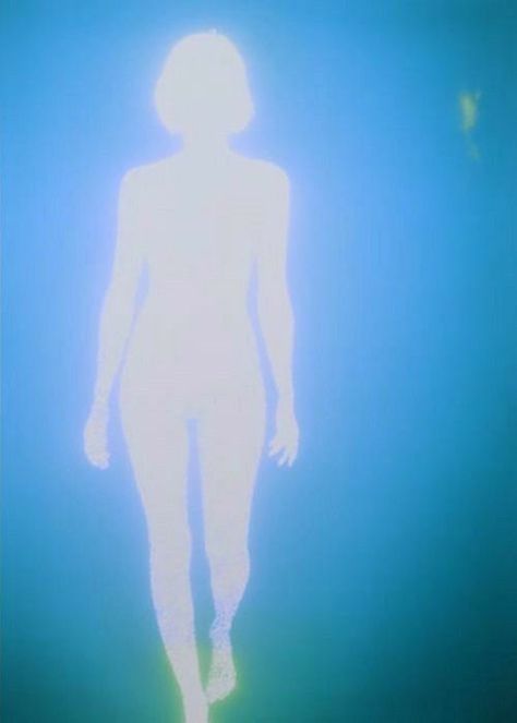 a person standing in the water with their back turned to the camera and light shining on them