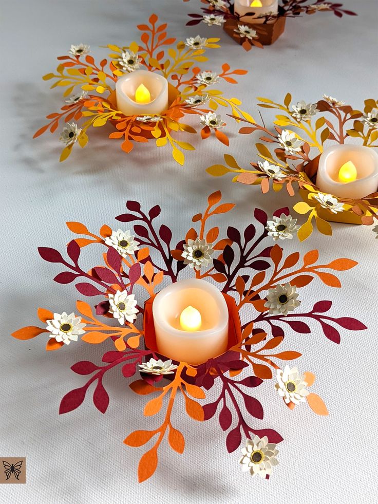 paper flowers and candles are arranged on a white tablecloth with orange, yellow, and red leaves