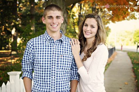 a young man and woman standing next to each other in front of a white picket fence