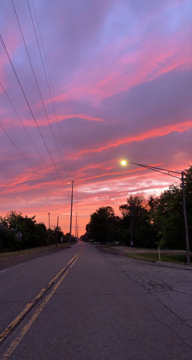 the sun is setting on an empty street with power lines in the distance and telephone poles to the side