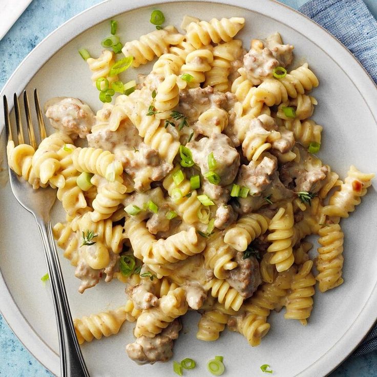 a white plate topped with pasta and meat covered in sauce next to a silver fork