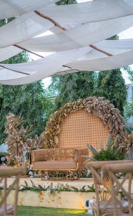 an outdoor seating area with white draping and greenery on the walls, along with wicker furniture