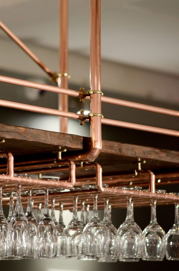 several wine glasses are lined up in front of a metal rack with copper piping