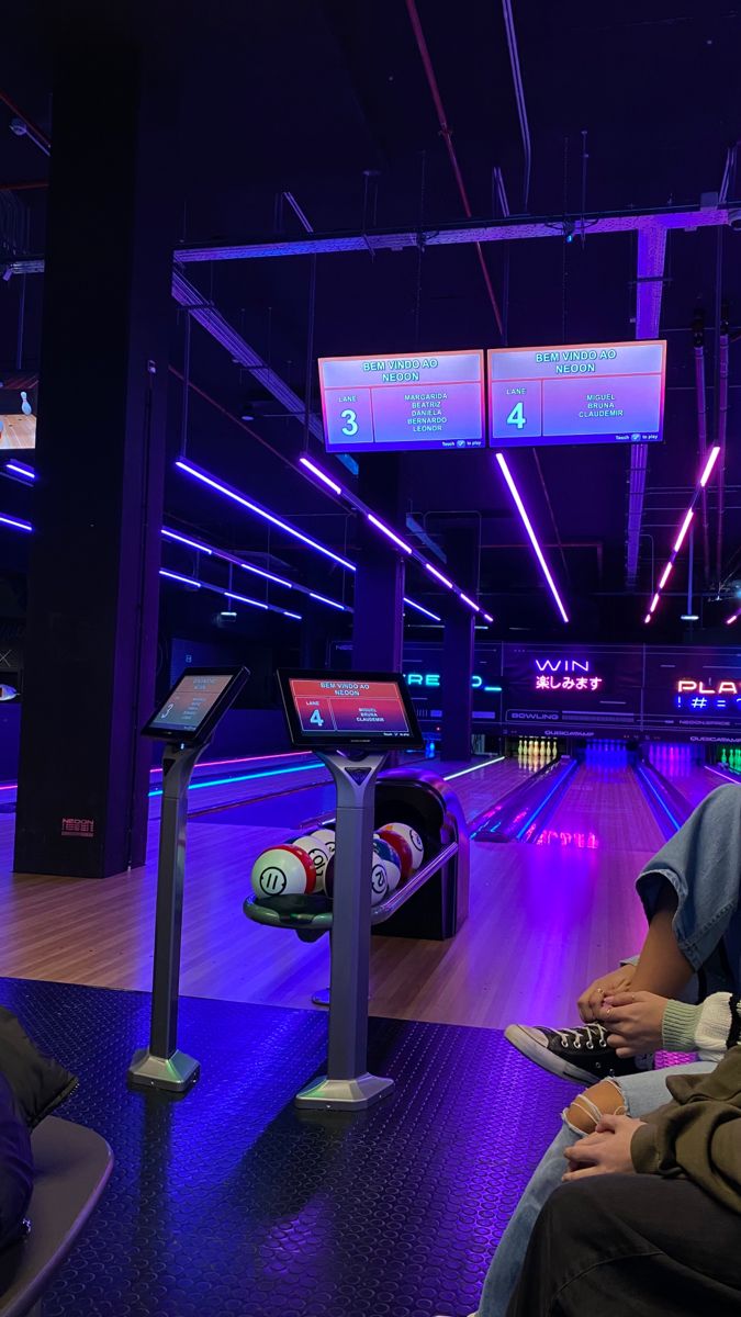 two people are sitting at a bowling alley and one person is holding a remote control