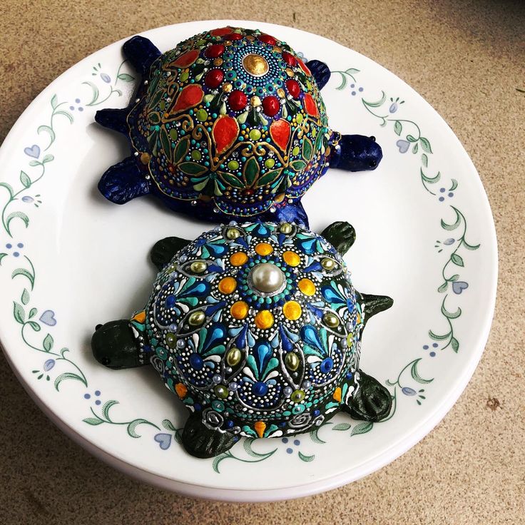 two ceramic turtle figurines sitting on top of a white plate with floral designs