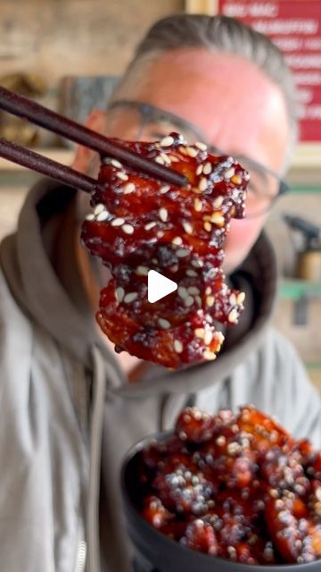 a man is holding up chopsticks to eat food from a black bowl with red sauce on it