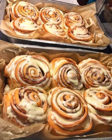 two pans filled with cinnamon rolls sitting on top of a counter next to each other