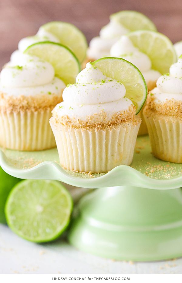 lime cupcakes with white frosting on a green cake platter surrounded by lime slices