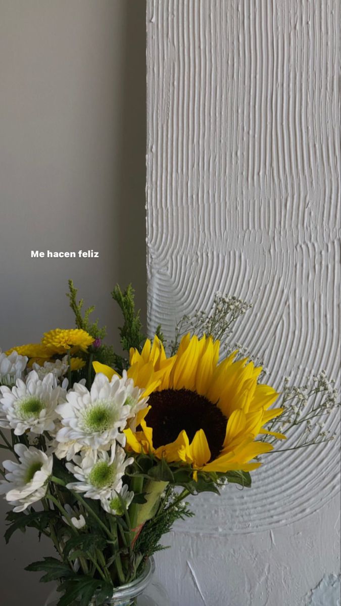 sunflowers and daisies in a vase on a table next to a wall