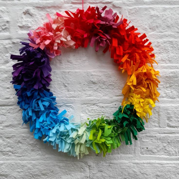 a rainbow colored paper wreath on a white brick wall