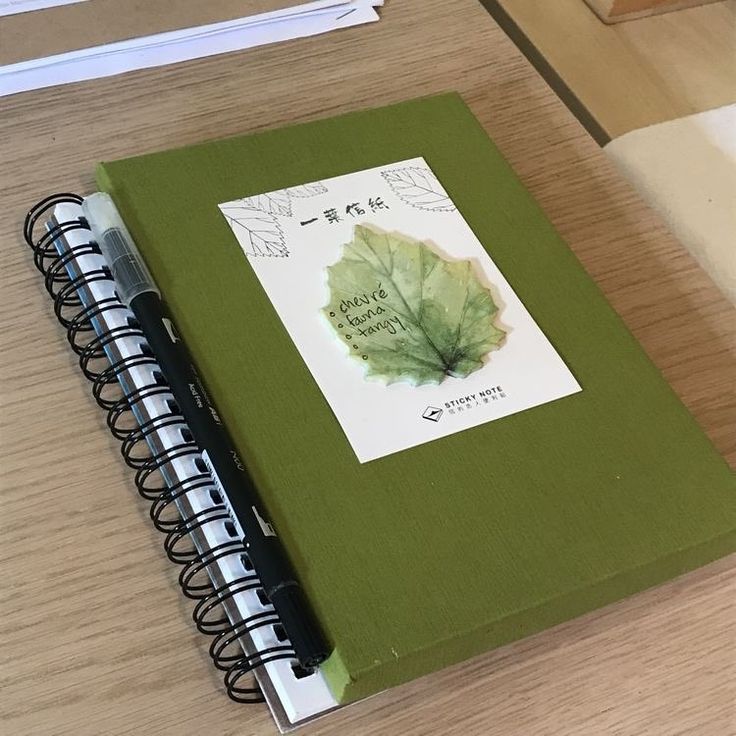 a book with a leaf on it sitting on a table next to a pen and paper