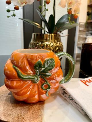 a ceramic pumpkin mug sitting on top of a wooden table next to a vase with flowers