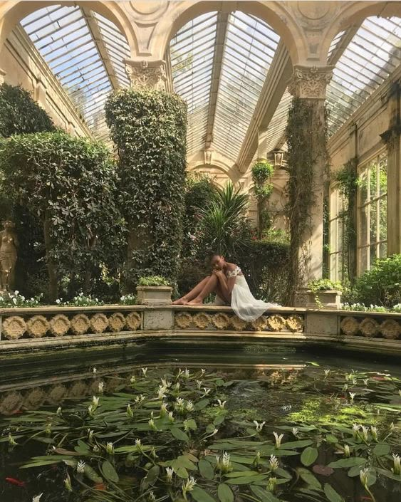 a bride and groom are sitting on the edge of a pond in a glass house