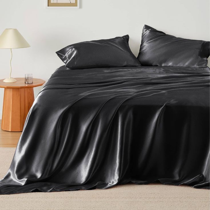 a bed with black sheets and pillows in a room next to a lamp on a table