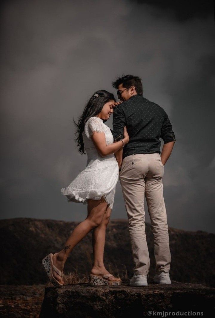 a man and woman standing next to each other on top of a hill under a cloudy sky