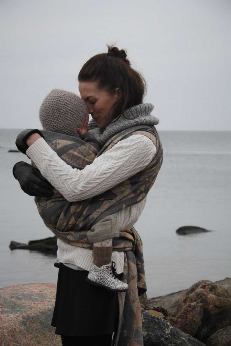 a woman holding a baby on top of a rocky beach