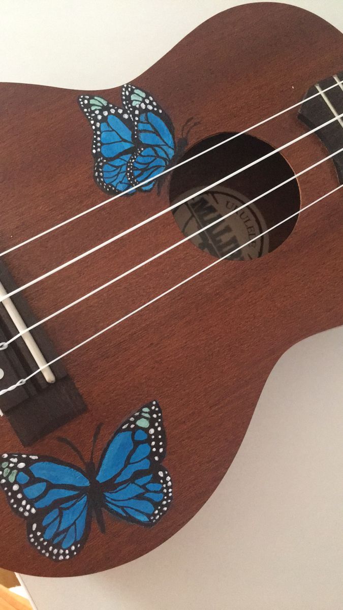 a ukulele with blue butterflies painted on the fret and strings, sitting on a table