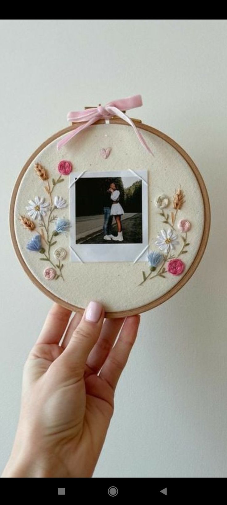 a person holding up a small photo frame with flowers on it and a pink ribbon around the edge