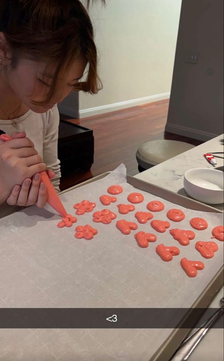 a woman is cutting out cookies on a table with a carrot in front of her