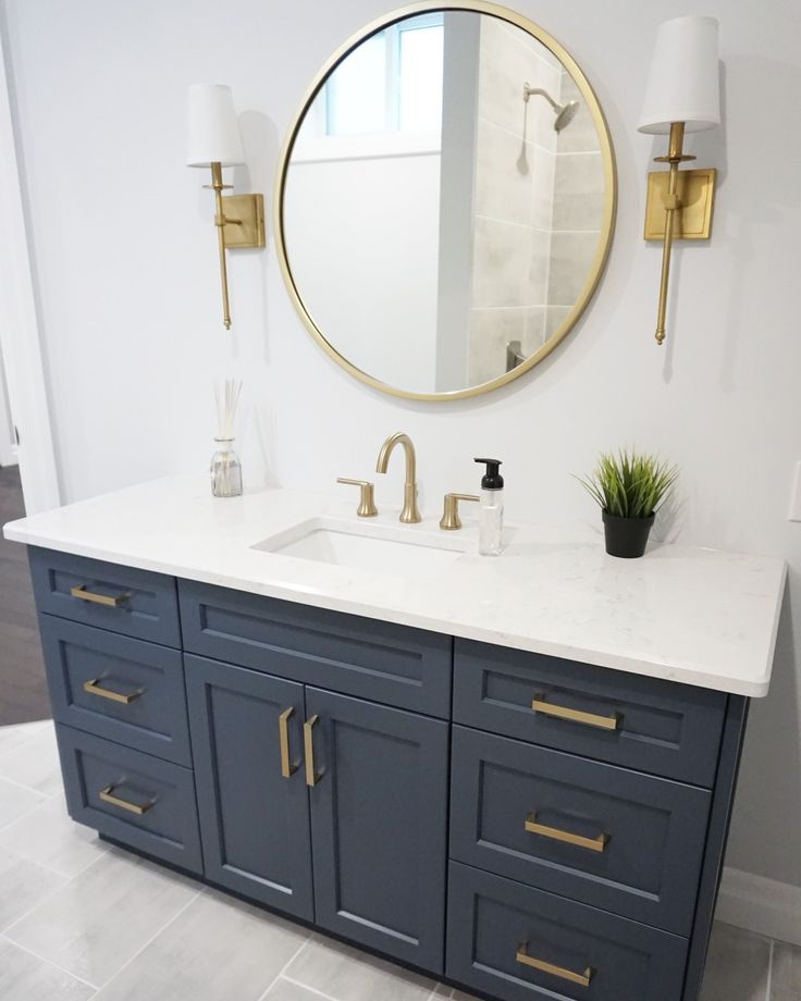 a bathroom vanity with two sinks and a large round mirror above it, in front of a white wall