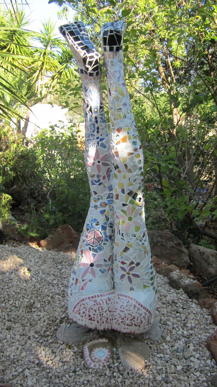 a statue made out of glass sitting on top of a gravel covered ground with trees in the background