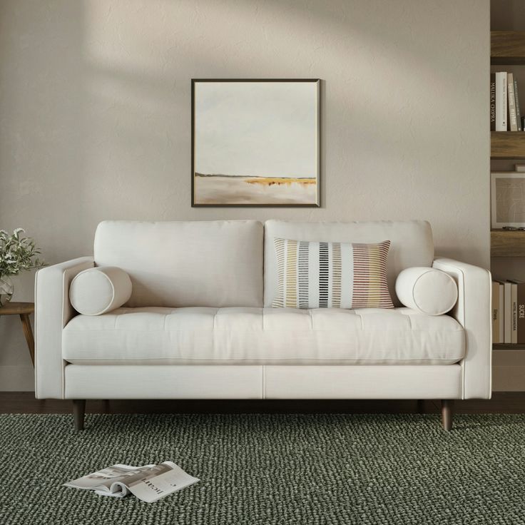 a white couch sitting on top of a green rug next to a wooden table and bookshelf