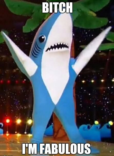 a blue and white shark mascot standing in front of a stage with lights behind it