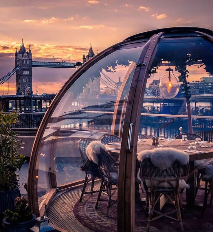 an outdoor dining area with tables and chairs in front of the city skyline at sunset