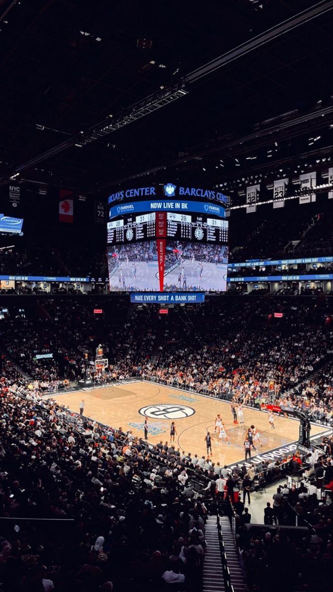 an indoor basketball game is being played on a big screen in the middle of a stadium