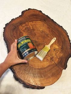 a person holding a paint brush on top of a wooden slice