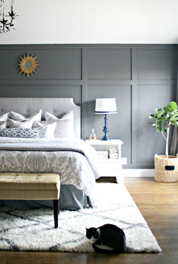 a bedroom with gray walls and white bedding in the center, along with a black cat on the floor