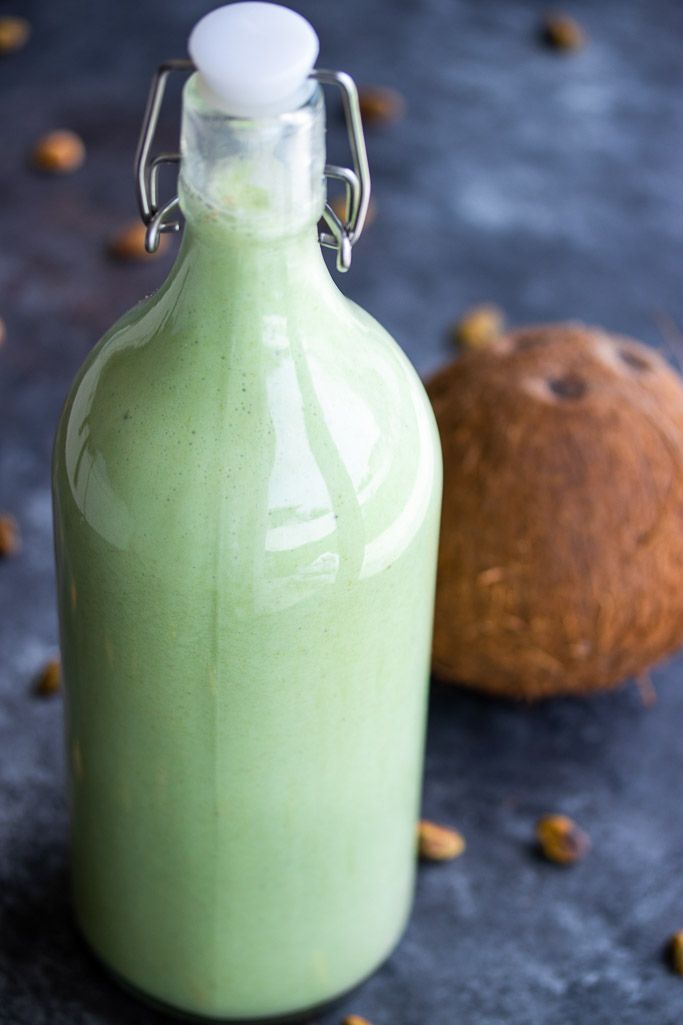 there is a green drink in a glass bottle next to a whole coconut on the table