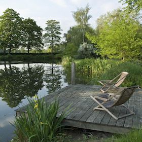 a lawn chair sitting on top of a wooden dock next to a lake and trees