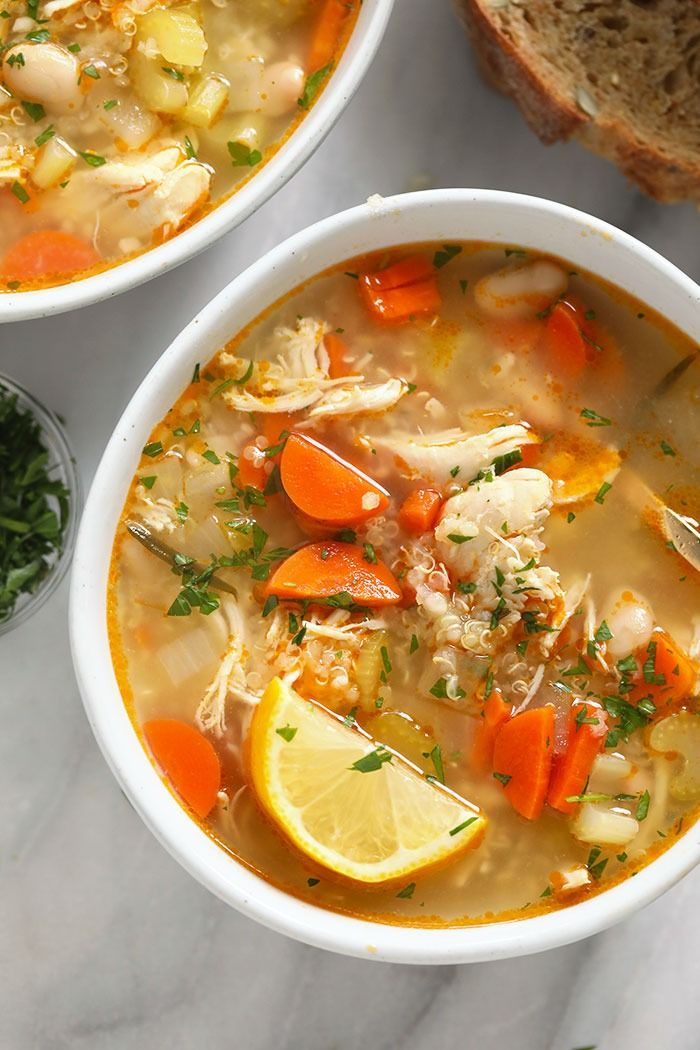 two bowls of chicken soup with lemon, carrots and parsley on the side