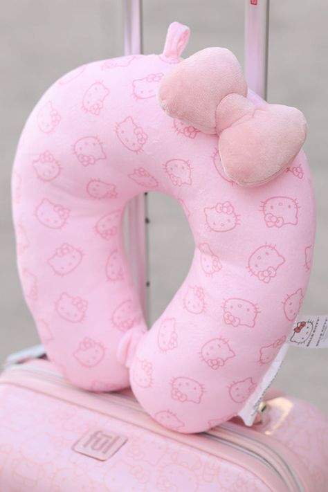 a pink hello kitty travel pillow sitting on top of a suitcase