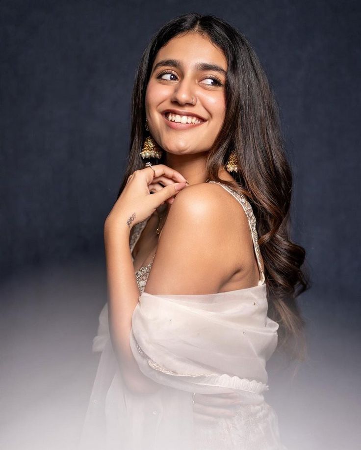 a woman in a white dress posing for the camera with her hand on her shoulder