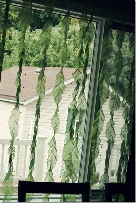 green leaves hanging from the side of a window next to a table and chair in front of a white house