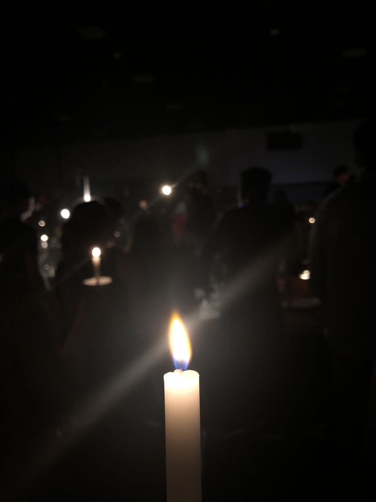 a candle lit in the dark with people standing around