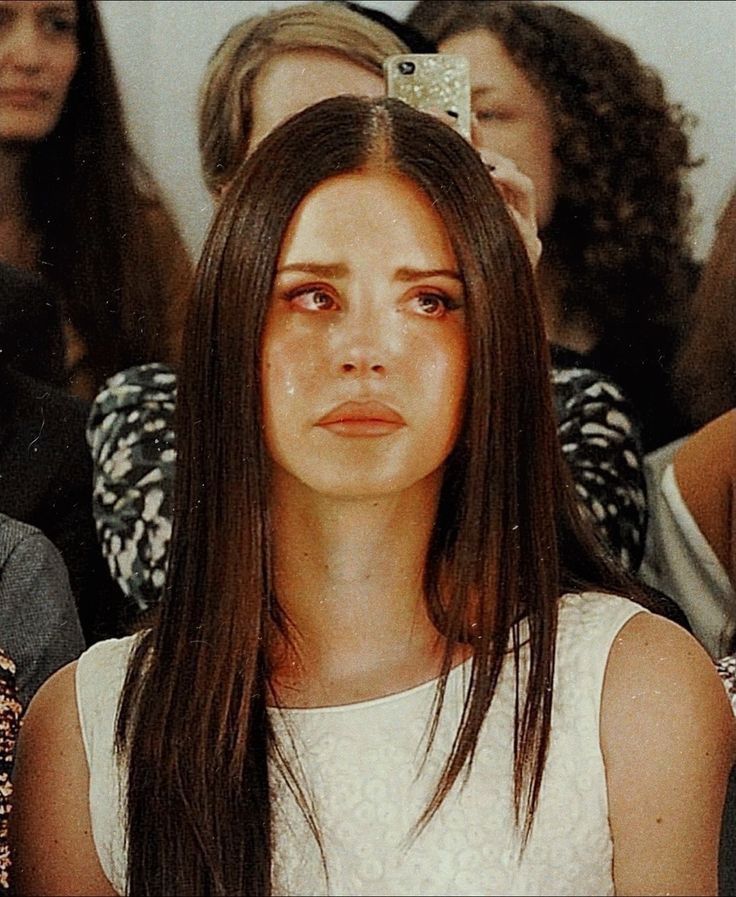 a woman with long brown hair sitting in front of a group of people looking at the camera