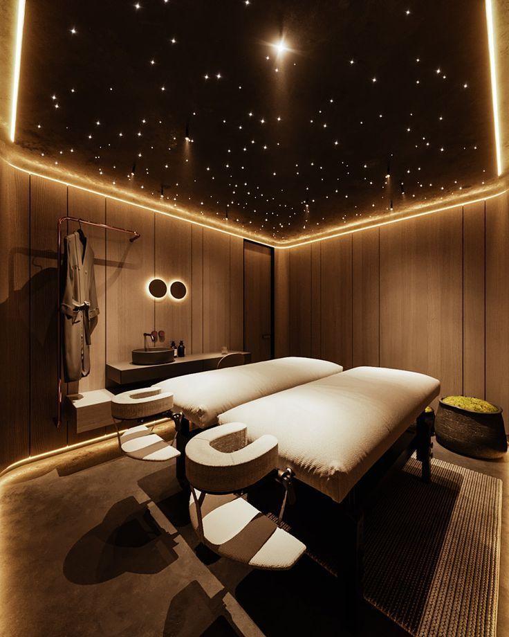 a spa room with two massage tables and lights on the ceiling above it, in front of a large mirror