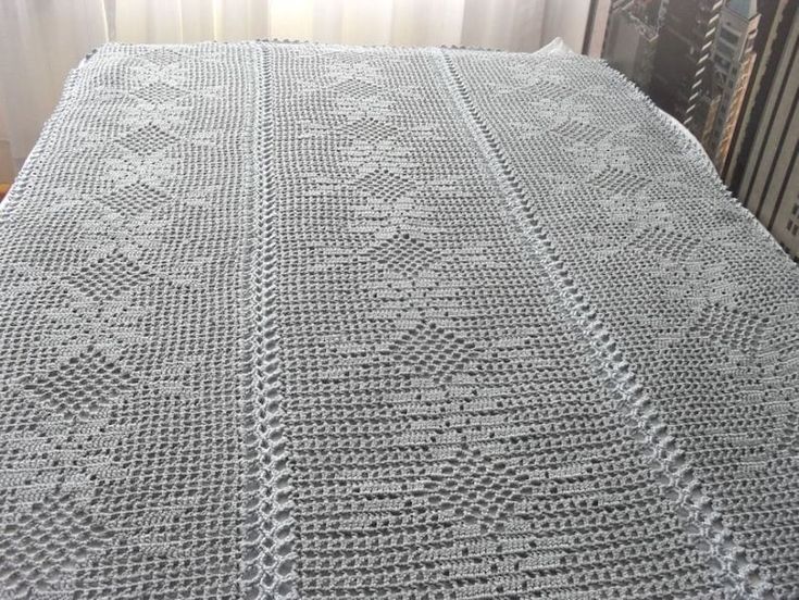 a white crocheted bed spread sitting on top of a wooden floor next to a window