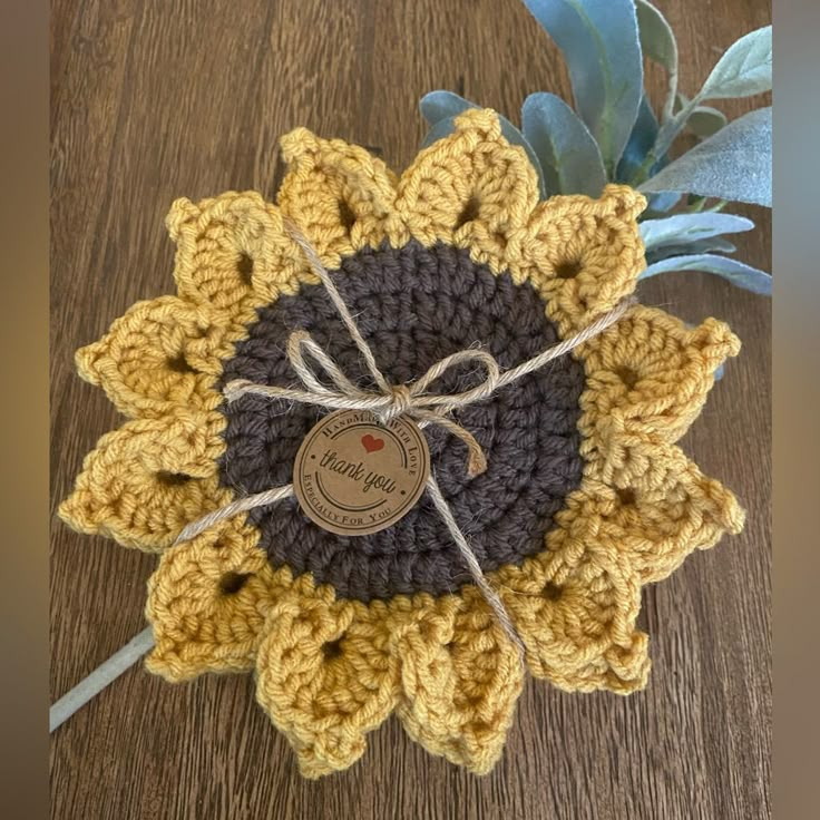 a crocheted sunflower with a tag attached to it on a wooden surface